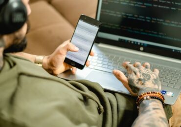 guy with tatoos holding his phone and laptop