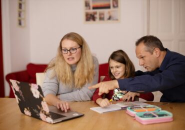 A mother and father helping their daughter with schoolwork on a laptop, symbolizing how families engage with technology for education and everyday life.