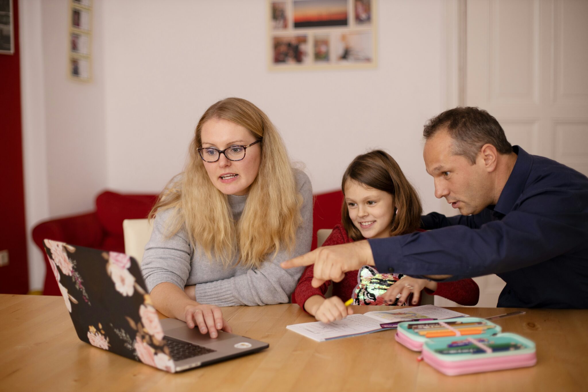 A mother and father helping their daughter with schoolwork on a laptop, symbolizing how families engage with technology for education and everyday life.